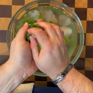Strizzatura manuale energica del mix di erbe per eliminare completamente l'acqua in eccesso prima di creare l'olio al basilico fatto in casa.