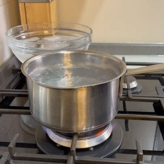 Pentola di acqua bollente sul fuoco e ciotola con acqua e ghiaccio per la preparazione dell'olio alle erbe ricetta veloce.