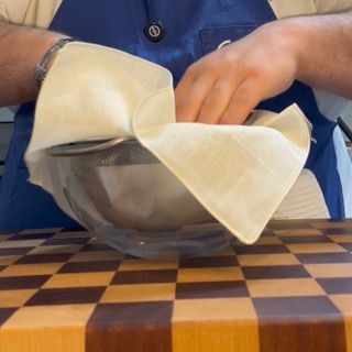 Posizionamento del colino foderato in lino sopra una ciotola capiente per raccogliere l'olio alle erbe.