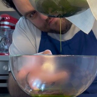 Dettaglio dell'olio alle erbe aromatiche dal colore verde brillante filtrato all'interno della ciotola.