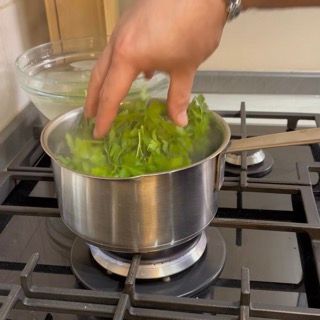 Immersione del prezzemolo fresco nell'acqua bollente per la nostra olio al prezzemolo ricetta.