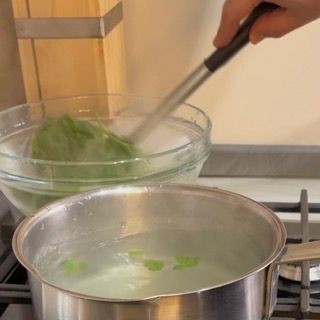 Passaggio istantaneo del prezzemolo nella ciotola con ghiaccio per ottenere un olio al prezzemolo veloce e brillante.