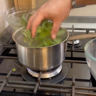 Inserimento delle foglie di basilico nell'acqua bollente per scoprire l'olio al basilico come si fa.