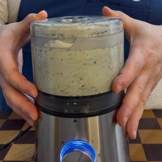 Consistenza finale della salsa alle erbe verde chiara, liscia e vellutata all'interno del boccale.