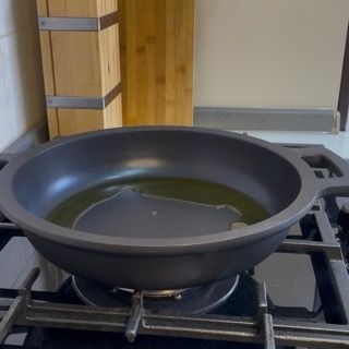 Scaldamento dell'olio extravergine d'oliva in una padella capiente sul fuoco.