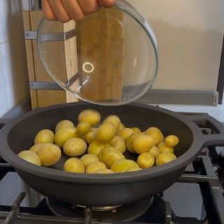 Inserimento delle patate novelle nella padella calda con l'olio per iniziare la cottura delle patate arrosto.