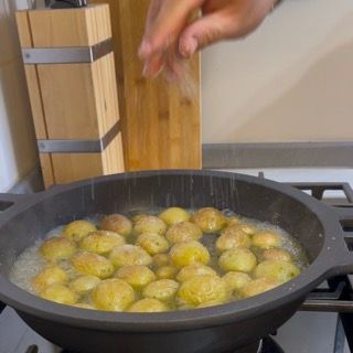 Distribuzione manuale di sale fino e pepe nero macinato sulle patate novelle in padella.