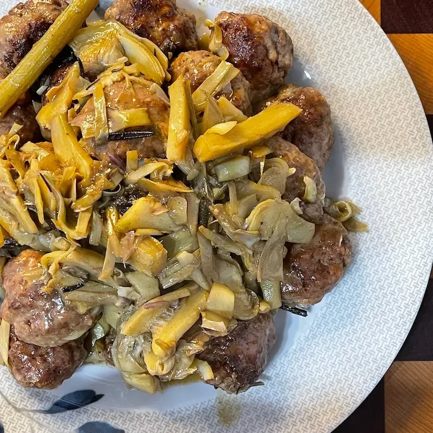 Padella fumante con polpette di carne morbide in bianco cotte con carciofi a spicchi e un sughetto cremoso e saporito