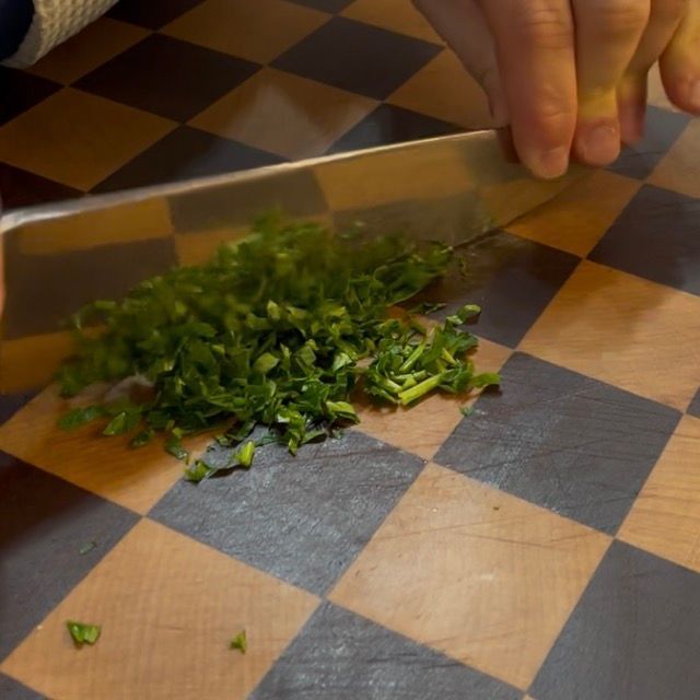 Tritatatura fine del prezzemolo fresco sul piano di lavoro da cucina.