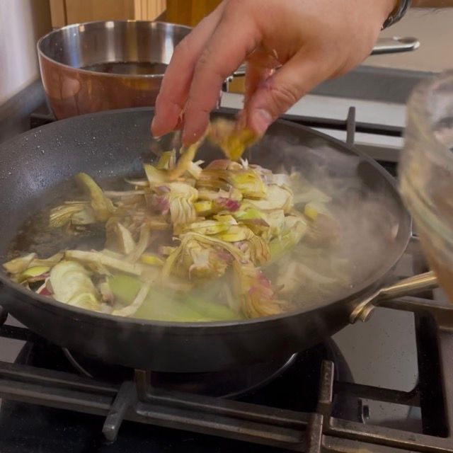 Inserimento dei carciofi affettati direttamente nella padella con il fondo di cottura della carne.