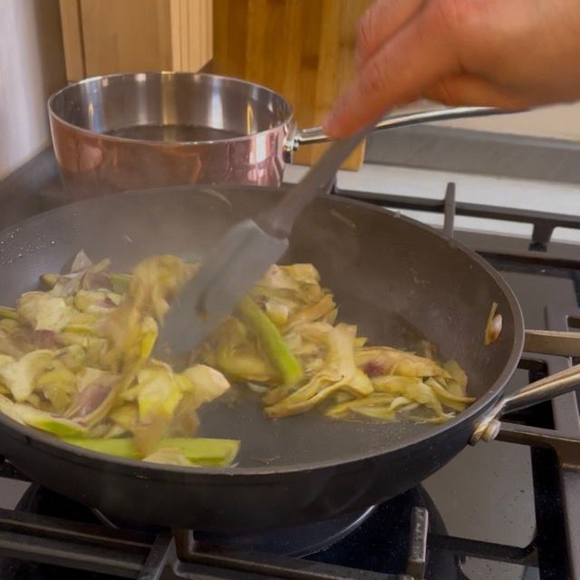 Salatura e mescolamento dei carciofi con un cucchiaio di legno in padella.
