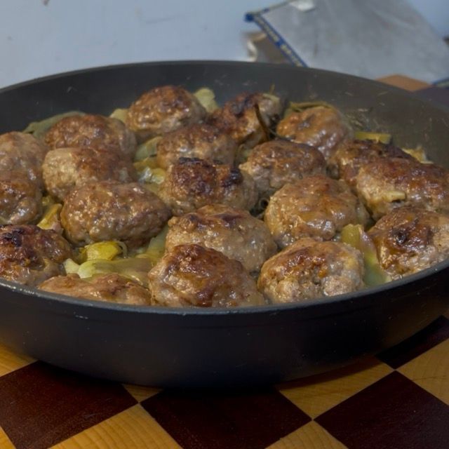 Porzione di polpette succulente e carciofi morbidi serviti su un piatto da portata.