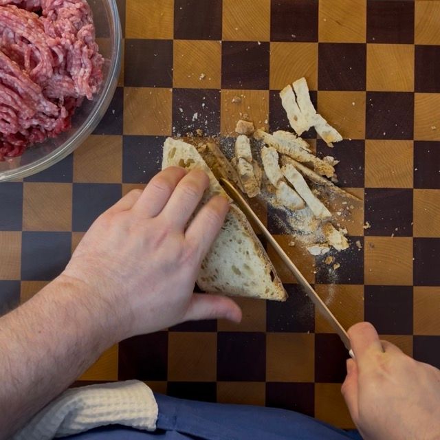Taglio del pane avanzato a cubetti su un tagliere di legno per la ricetta polpette di carne della nonna