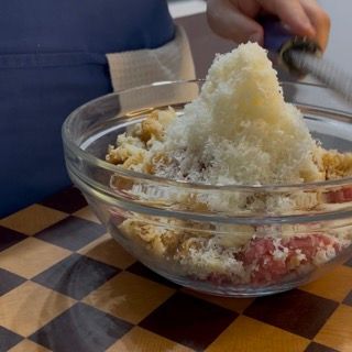 Versamento di una dose generosa di grana o parmigiano grattugiato sopra gli ingredienti per ottenere polpette di carne della nonna morbide.