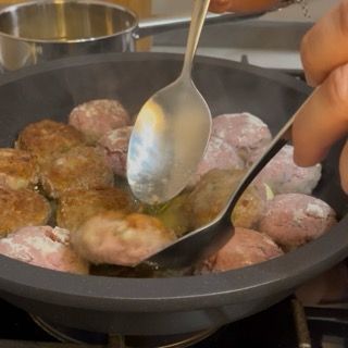 Rotazione delle polpette con una pinza da cucina per mostrare la crosticina dorata in superficie.