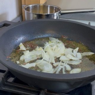 Inserimento delle fettine di cipolla sottili nel fondo di cottura caldo.