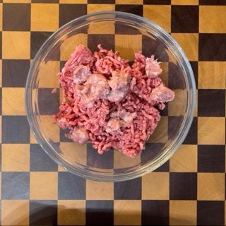 Aggiunta della salsiccia sgranata alla carne macinata di vitella nella ciotola per la ricetta polpette di carne della nonna.
