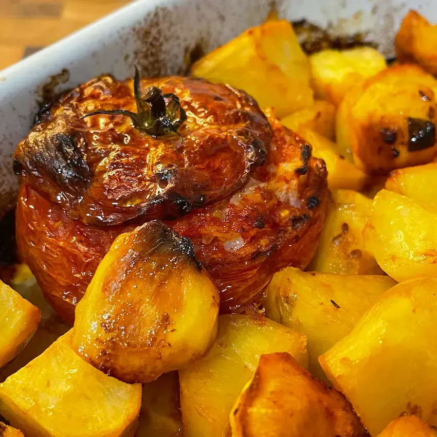 Dettaglio di un pomodoro con riso alla romana aperto, ripieno di riso saporito e servito con patate al forno croccanti.