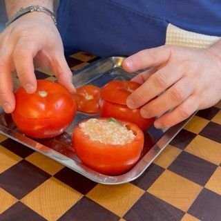 Vista ravvicinata di tutti i pomodori ripieni chiusi con il loro coperchio naturale, pronti per la teglia.