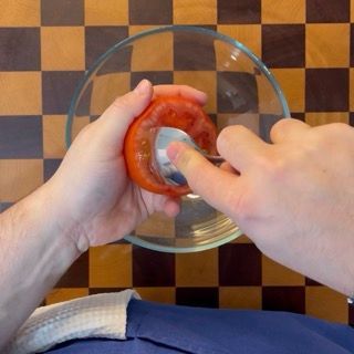 Inizio dello scavo della polpa interna del pomodoro con un cucchiaio d'acciaio per la farcitura.