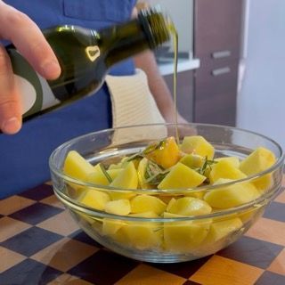 Dettaglio delle patate ben cosparse di salsa di pomodoro, olio e rosmarino prima della cottura.