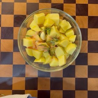 Mani che mescolano energicamente le patate nella ciotola per distribuire il condimento in modo omogeneo.