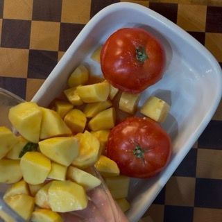 Inserimento degli spicchi di patate condite negli spazi vuoti tra i pomodori nella teglia.