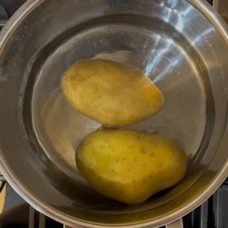 Selezione di patate medio grandi immerse in una pentola con acqua fredda per la ricetta purè di patate.