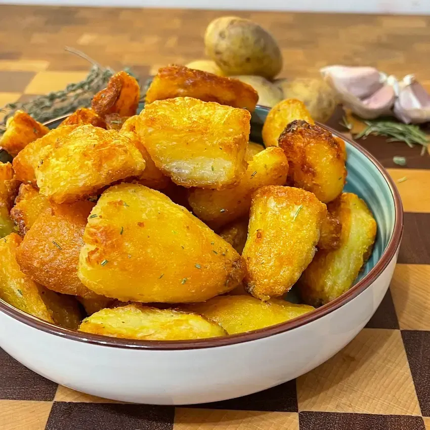 primo piano delle Patate al forno croccanti e dorate in un piatto, condite con rosmarino fresco e sale grosso.
