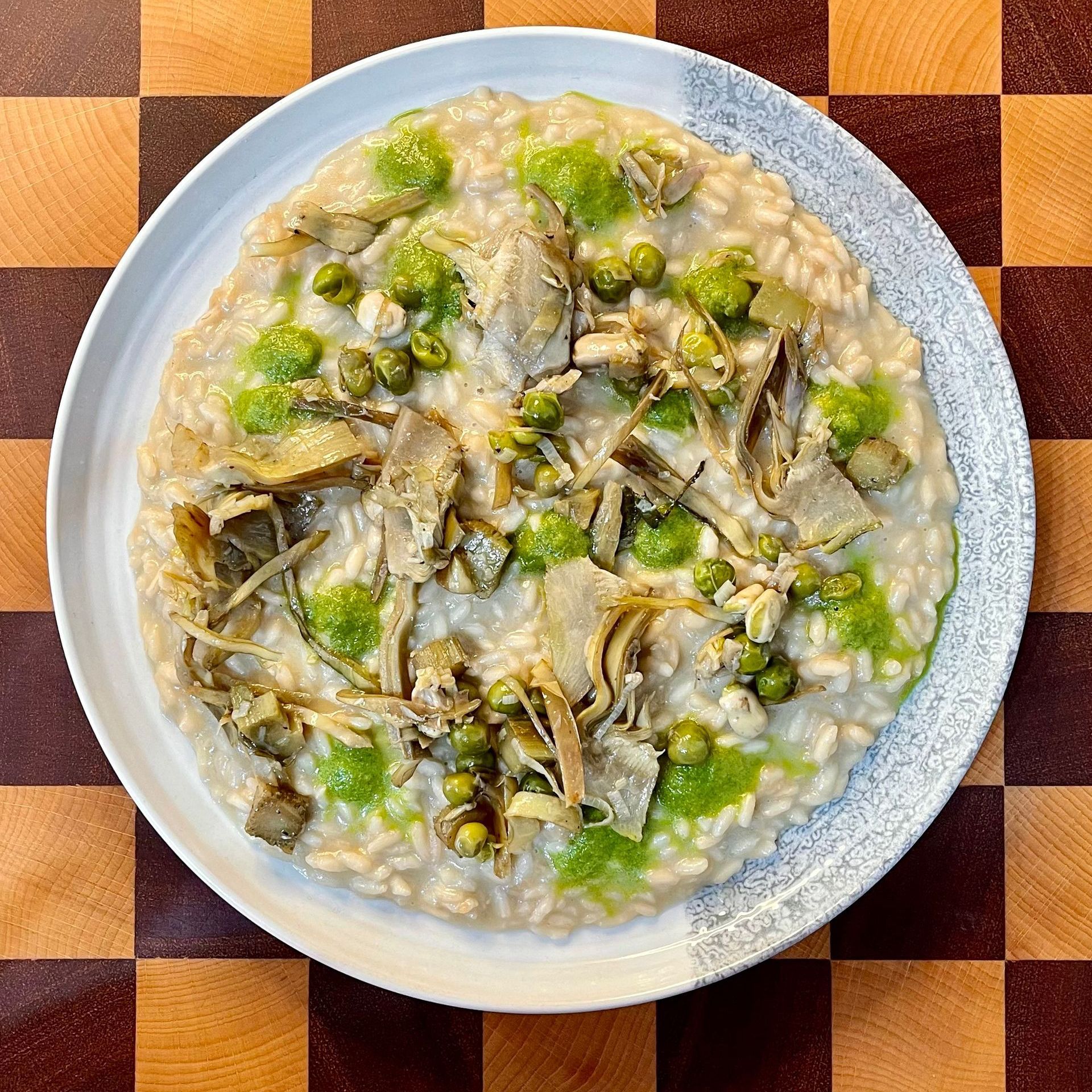 un piatto di risotto alla vignarola è appoggiato su un tavolo di legno 