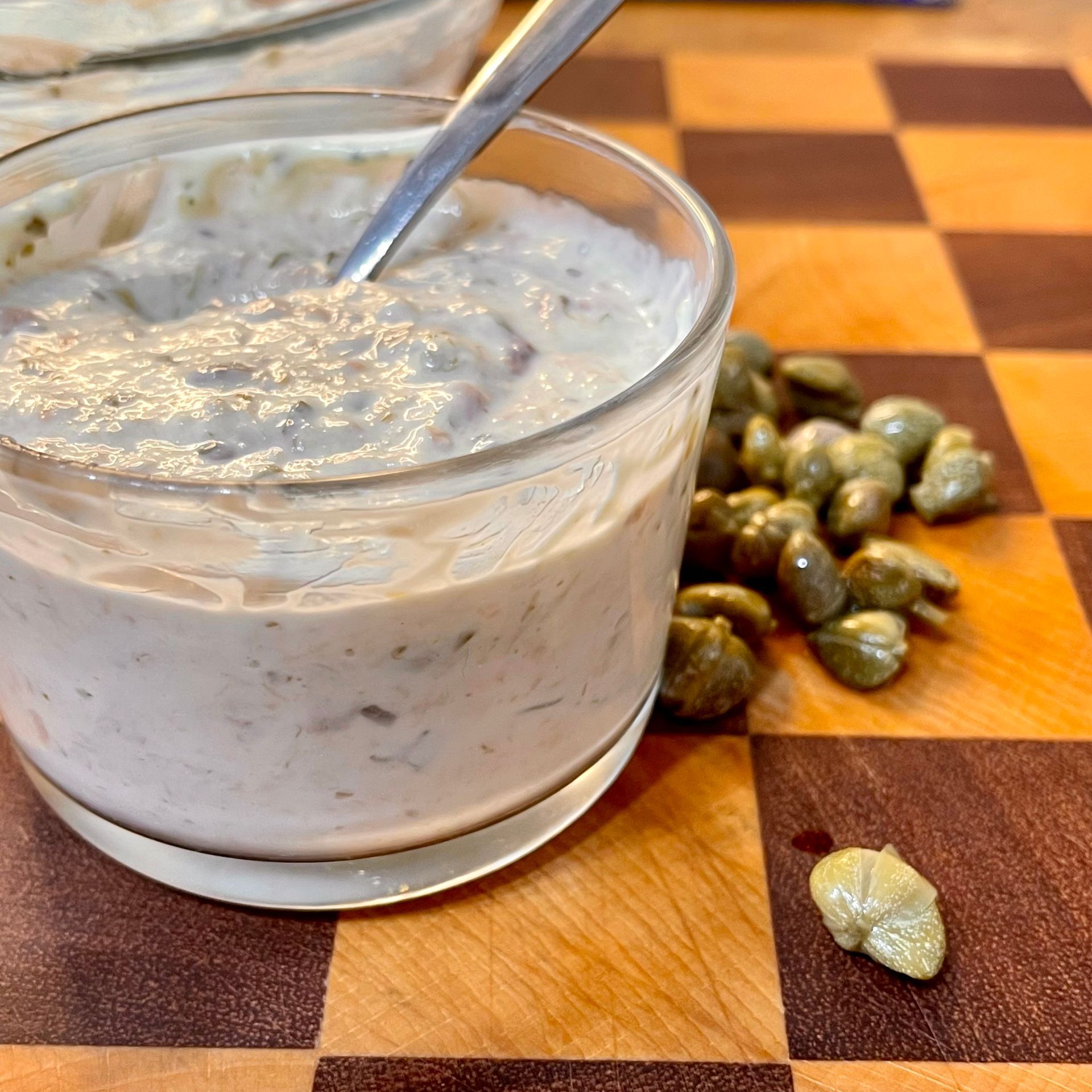 Primo piano della Salsa tonnata cremosa fatta in casa, servita in una ciotola bianca con capperi.