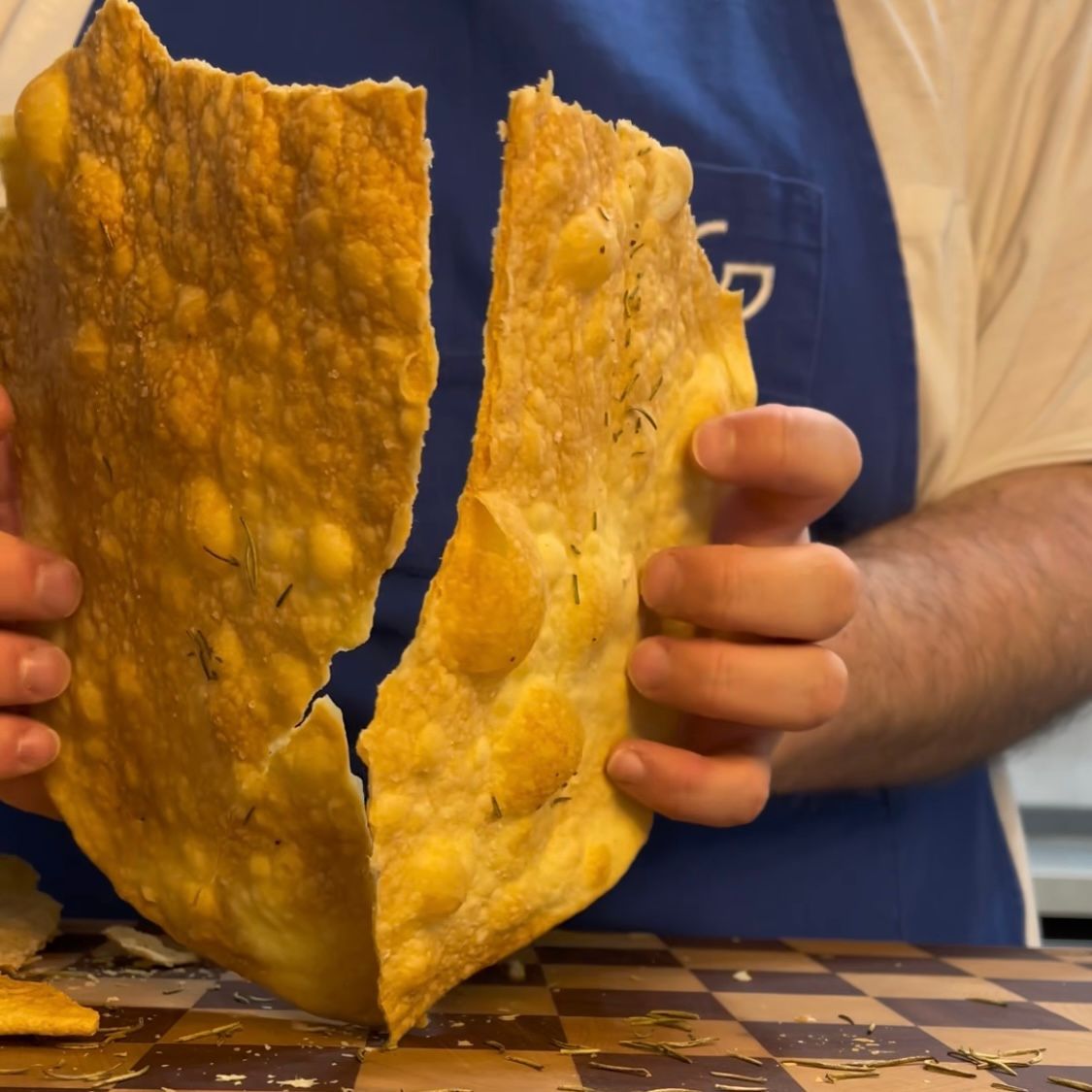 Un uomo con un grembiule blu tiene in mano un grosso pezzo di cibo