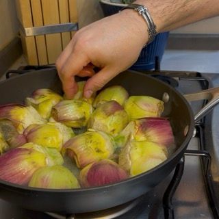 Carciofi disposti a raggiera in padella, con la parte tagliata verso il basso.