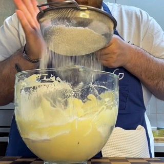 Setaccio di farina e fecola di patate sopra l'impasto spumoso della torta tiramisù facile.