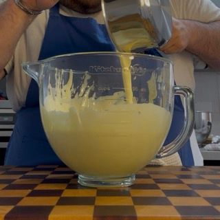 Versamento della gelatina sciolta nella montata principale di tuorli per la torta tiramisù ricetta.