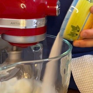 Aggiunta graduale dello zucchero negli albumi schiumati per la base della torta tiramisù con savoiardi.