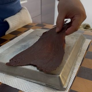 Adagiamento del telo di cioccolato scuro sulla cupola della torta tiramisù compleanno.