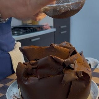 Copertura completa della torta tiramisù con i veli di cioccolato prima della spolverata finale.