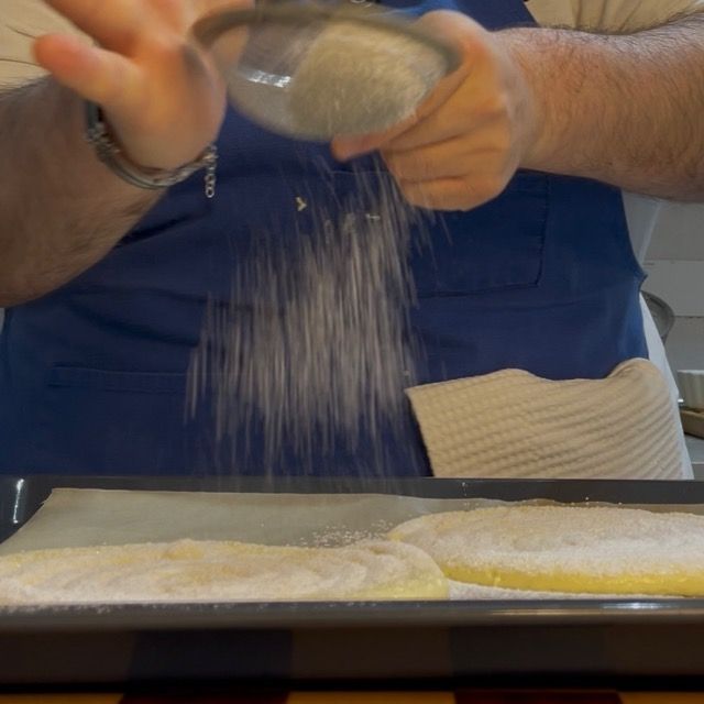 Spolverata abbondante di zucchero a velo sui dischi di pasta savoiardo prima di infornare.