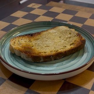 Tostatura di una fetta di pane cotto a legna in padella con olio e aglio per accompagnare il denso tzatziki.