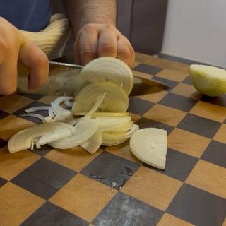Taglio a fettine sottili di una cipolla sul tagliere per il soffritto delle zucchine ripiene in padella.