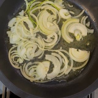 Inserimento delicato delle zucchine ripiene di carne nel tegame caldo con il soffritto di cipolla profumato.