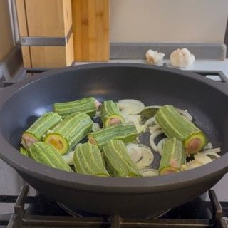 Aggiunta delle polpettine di carne negli spazi vuoti del tegame insieme alle zucchine romanesche ripiene.
