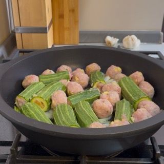 Distribuzione uniforme di zucchine e polpettine nel tegame e regolazione di sale e pepe per insaporire.