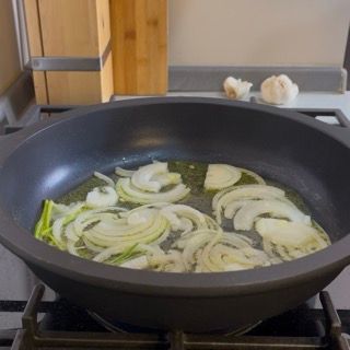 Aggiunta della cipolla affettata e dei gambi di prezzemolo per insaporire il fondo delle zucchine al sugo.