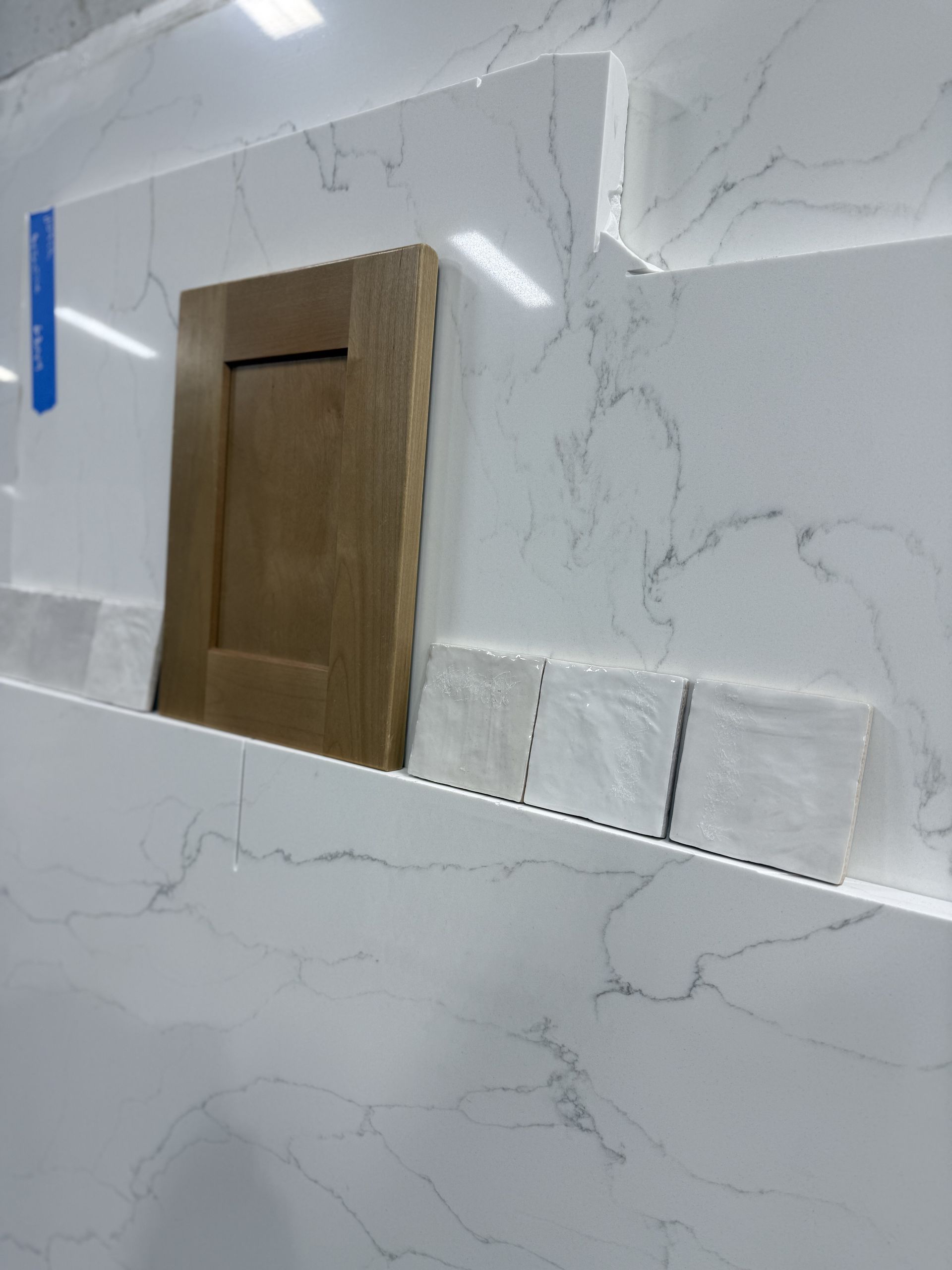 White marble-tiled wall with a wooden door panel and blue protective tape in a bathroom or shower area