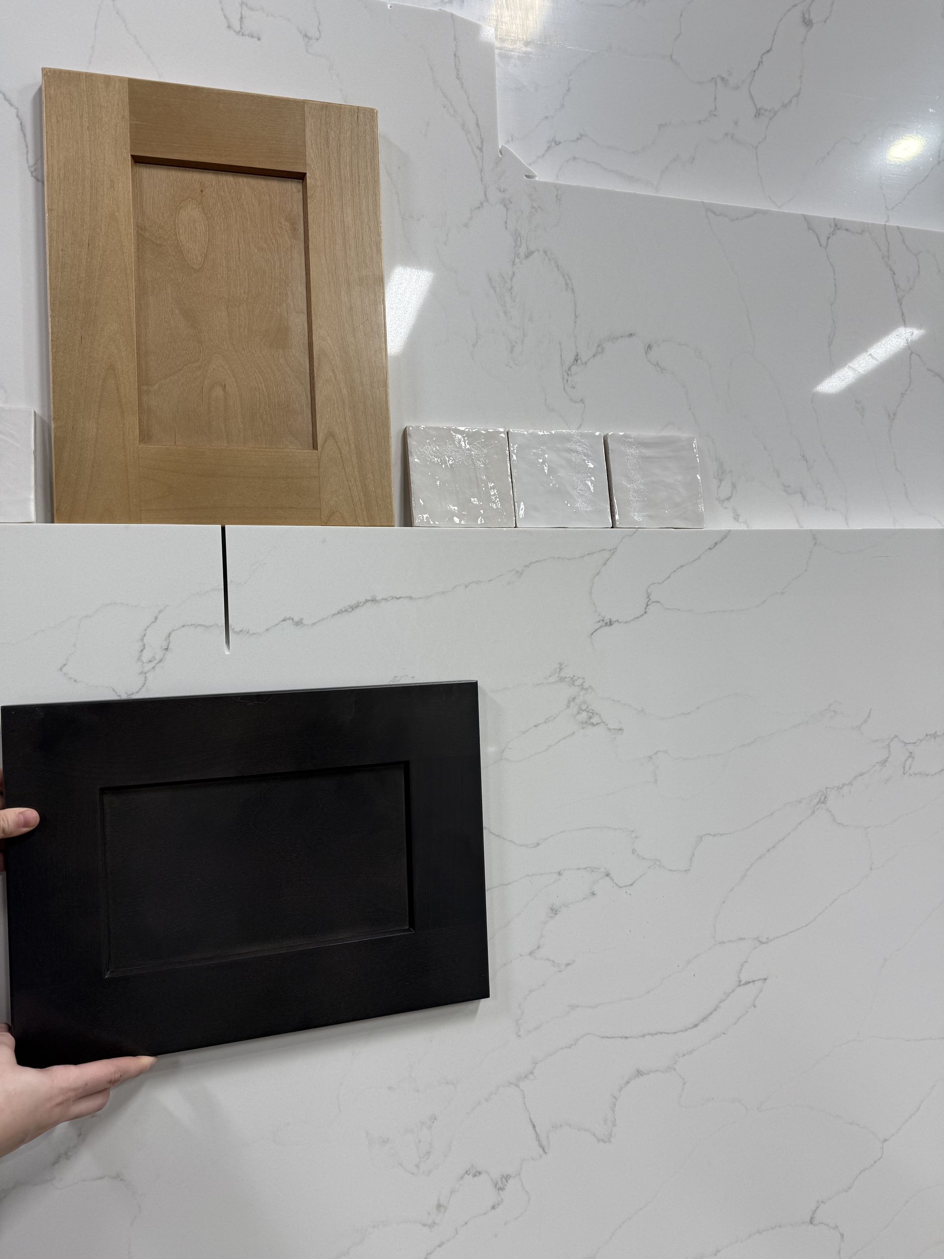 Hand holding a black rectangular panel next to a beige panel on a marble wall sample board