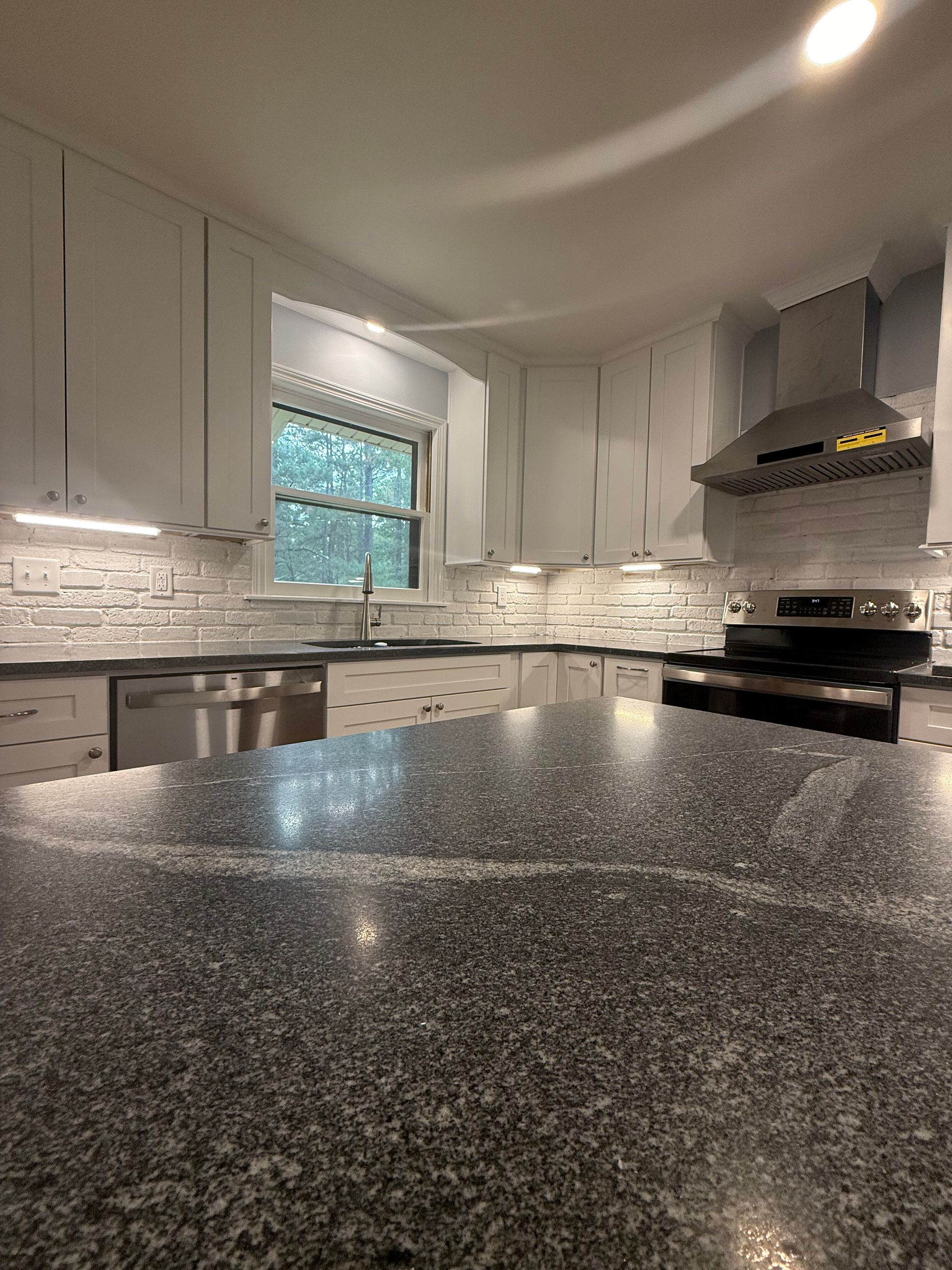 Bright modern kitchen with white cabinets, gray granite counters, and a window over the sink