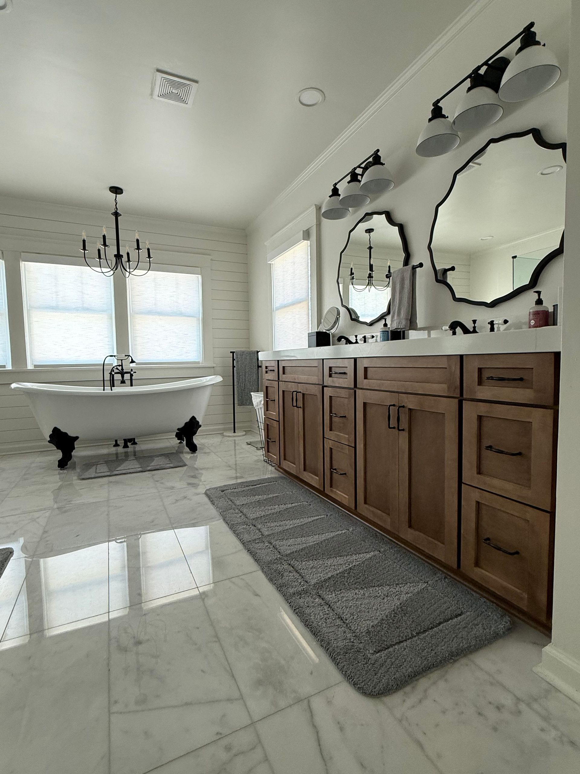 Bright bathroom with freestanding tub, double vanity, mirrors, and large window on glossy tile floor