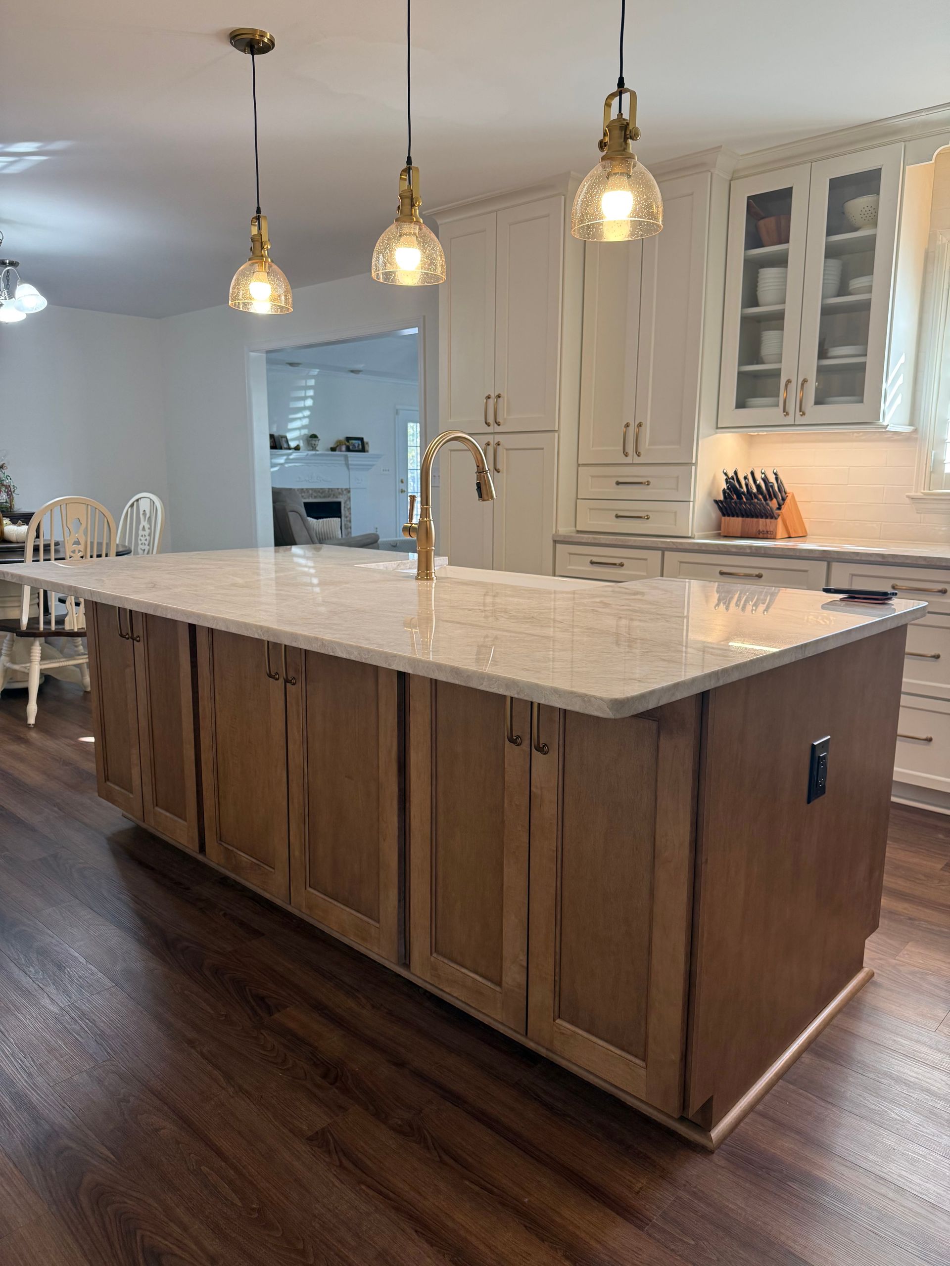 Modern kitchen with a large marble island, pendant lights, wood floors, and white cabinetry